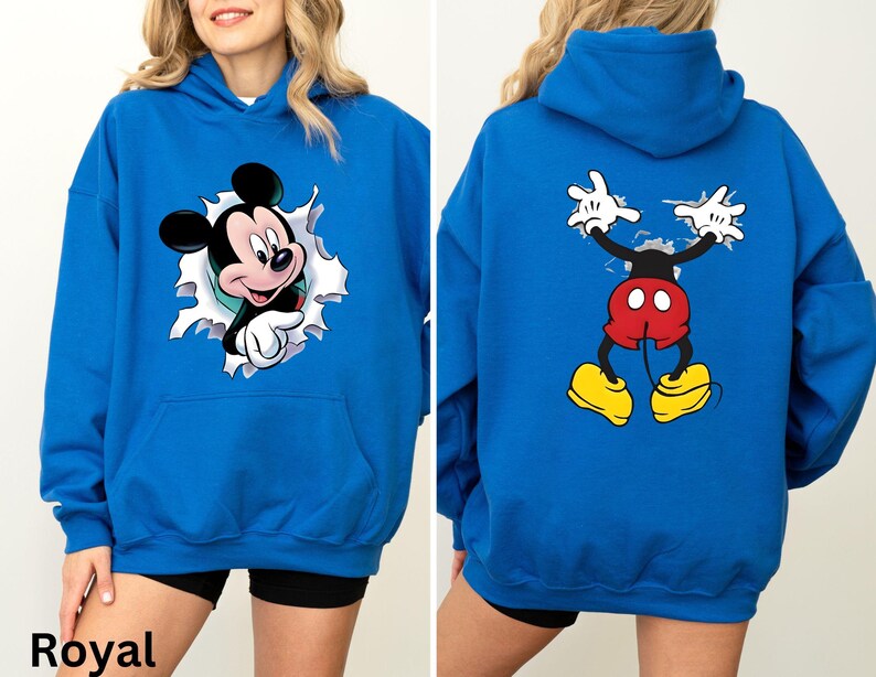 May include: Royal blue hoodie featuring Mickey Mouse. The front of the hoodie shows Mickey breaking through a torn white background. The back of the hoodie displays Mickey's full body, with his arms raised. The hoodie has a front pocket.
