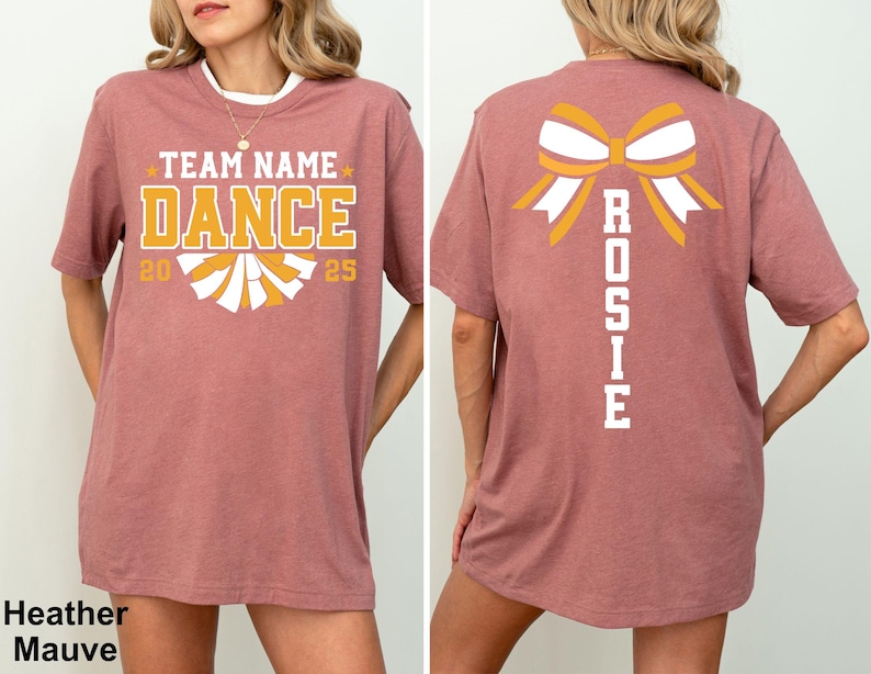 May include: Heather mauve t-shirt with "TEAM NAME DANCE 2025" in gold and white lettering on the front. The back features a bow graphic with the name "ROSIE" in white. The shirt has a crew neck and short sleeves.