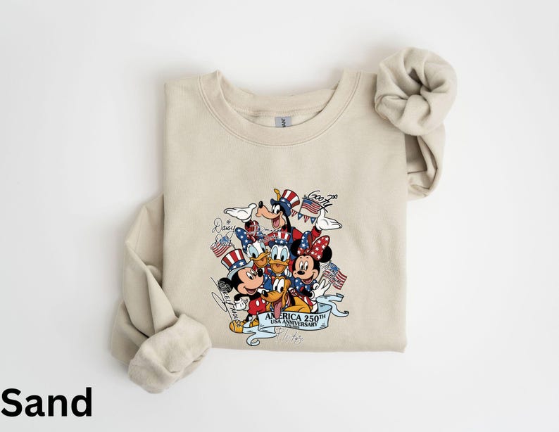 Puede incluir: Sudadera de color arena con un gr&aacute;fico colorido de personajes de Disney, incluyendo Mickey y Minnie Mouse, Goofy y Donald Duck, celebrando el 250 aniversario de Am&eacute;rica. El dise&ntilde;o incorpora elementos patri&oacute;ticos como banderas y sombreros del T&iacute;o Sam.