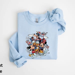 Puede incluir: Sudadera azul claro con un dise&ntilde;o de Mickey Mouse, Minnie Mouse, Donald, Goofy y Pluto con atuendos patri&oacute;ticos. El dise&ntilde;o incluye banderas americanas y el texto "America 250th Anniversary".