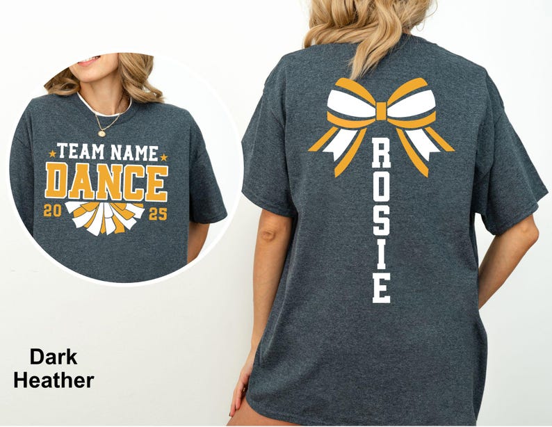 May include: Dark heather gray t-shirt with a cheerleading design. The front features the text "TEAM NAME DANCE 2025" in yellow and white. The back displays a bow graphic and the name "ROSIE" in white. A perfect tee for cheerleading.