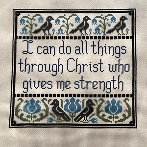 May include: Cross-stitch artwork with the text "I can do all things through Christ who gives me strength." The design features black birds, blue flowers, and green leaves. The artwork is framed with a black border.