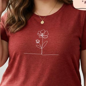May include: A maroon plus-size t-shirt with a white floral line drawing on the front. The shirt has a crew neck and short sleeves. Text on the image reads "PLUS SIZES 1X-4X *NOT UNISEX" and "True Plus Size Women's T-shirts."