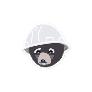 May include: A black bear wearing a white hard hat. The bear has blue eyes and a small orange nose.