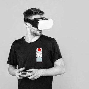 May include: A person wearing a black t-shirt with a red and white graphic design, holding a video game controller and wearing a virtual reality headset.