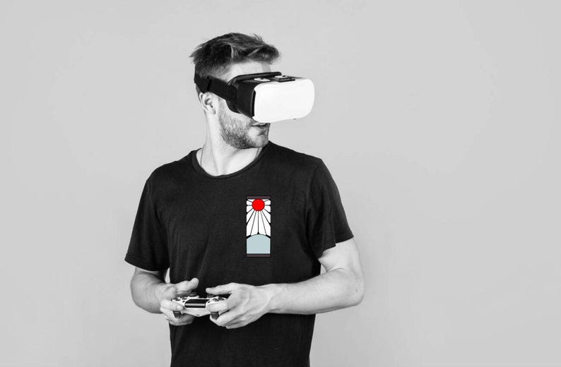 May include: A person wearing a black t-shirt with a red and white graphic design, holding a video game controller and wearing a virtual reality headset.
