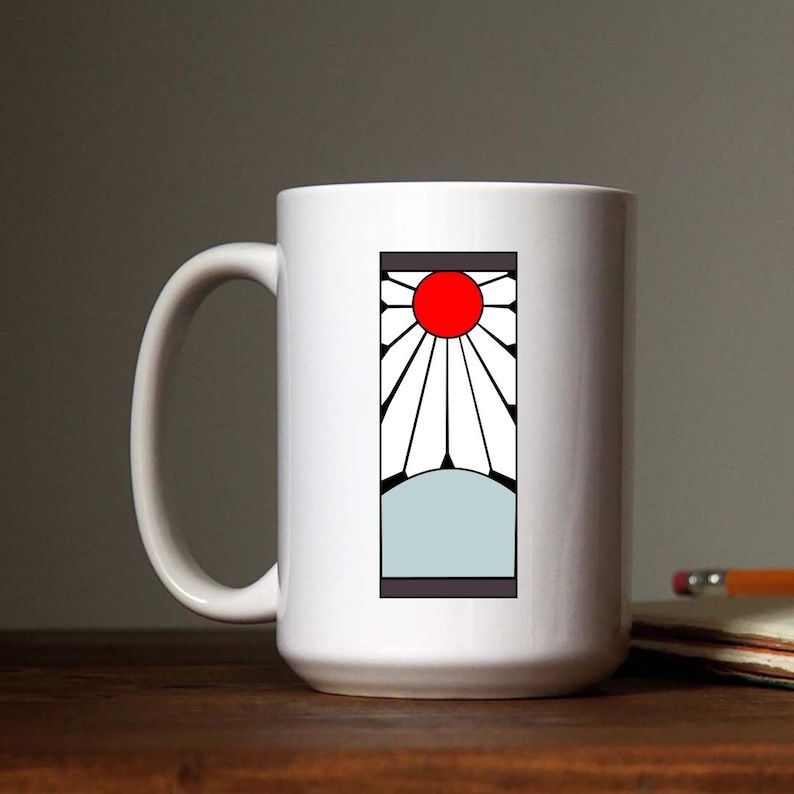 May include: White ceramic mug with a black and white graphic of a sun with a red center and a white background. The graphic is surrounded by a black border.