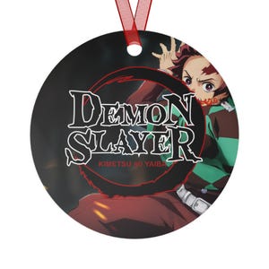 May include: Round ornament featuring a character from the anime Demon Slayer: Kimetsu no Yaiba. The character is wearing a red and green patterned haori and has red eyes. The text "Demon Slayer: Kimetsu no Yaiba" is written in black on a red circle.