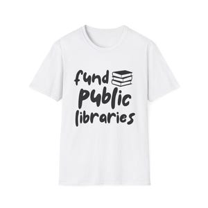 May include: White t-shirt with the phrase "fund public libraries" in black script. The design includes a stack of three books. The shirt is a classic crew neck style.