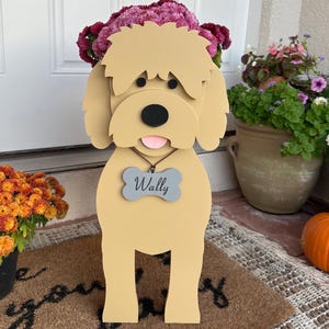 May include: A light brown wooden dog planter with a bone-shaped tag that says "Wally". The planter is decorated with pink flowers and has a black nose and pink tongue.