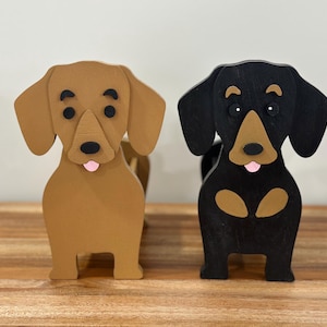 May include: Two wooden dachshund dog figurines. One is brown and the other is black. Both have pink tongues sticking out.
