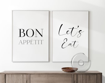 May include: Two framed wall art prints with white backgrounds. One reads "BON APPÉTIT" in black, the other says "Let's Eat". A wooden bowl and a clear glass vase sit on a wooden cabinet below.