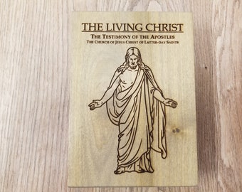 Op de afbeelding: Houten plaat met de tekst "THE LIVING CHRIST" en een illustratie van Jezus Christus. De tekst "THE TESTIMONY OF THE APOSTLES" en "THE CHURCH OF JESUS CHRIST OF LATTER-DAY SAINTS" zijn ook opgenomen.