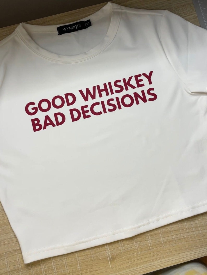 May include: White cropped t-shirt with the text "GOOD WHISKEY BAD DECISIONS" printed in red.