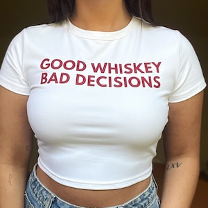May include: White cropped t-shirt with the text "GOOD WHISKEY BAD DECISIONS" printed in red.