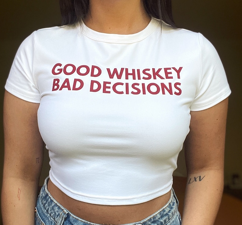 May include: White cropped t-shirt with the text "GOOD WHISKEY BAD DECISIONS" printed in red.