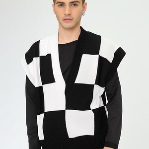 Könnte beinhalten: Eine schwarz-weiß karierte Strickweste mit V-Ausschnitt. Die Weste wird über einem schwarzen Langarmshirt getragen. Der Stil ist modern und lässig.