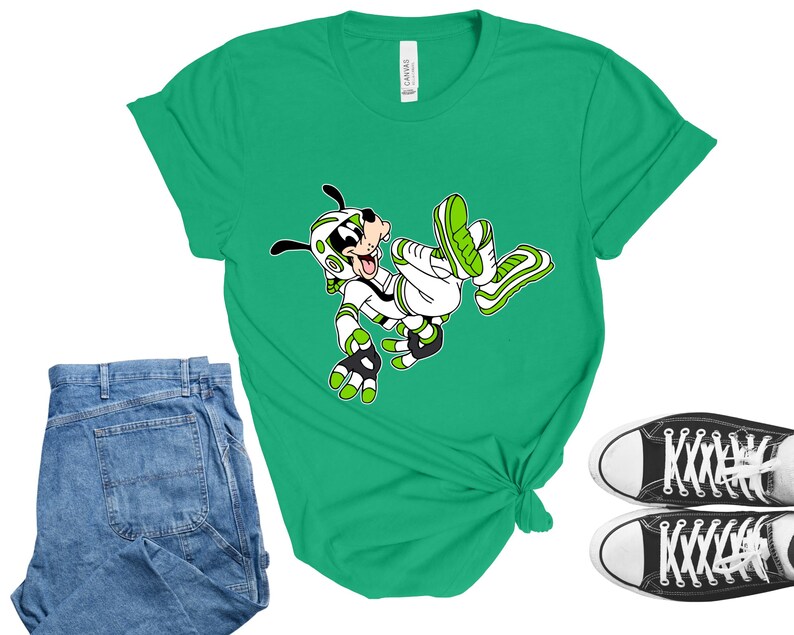 Peut inclure: Un t-shirt vert avec un personnage de dessin anim&eacute; v&ecirc;tu de blanc et de vert. L'image montre &eacute;galement un jean bleu et des baskets noires en toile avec des semelles et des lacets blancs. Le t-shirt est nou&eacute; &agrave; la taille.
