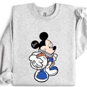 Peut inclure: Sweat-shirt gris clair avec un personnage de dessin anim&eacute; Mickey Mouse dans un design de combinaison spatiale. Le personnage porte une combinaison spatiale bleue et orange avec des gants et des bottes blancs. Le nom "Jack" est &eacute;crit sur l'oreille.