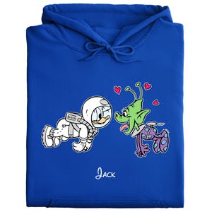 Peut inclure: Un sweat &agrave; capuche bleu roi avec une illustration de dessin anim&eacute; d'un canard astronaute et d'un extraterrestre vert avec des c&oelig;urs. Le mot "Jack" est &eacute;crit en cursive sous l'illustration. Le sweat &agrave; capuche a une capuche &agrave; cordon.