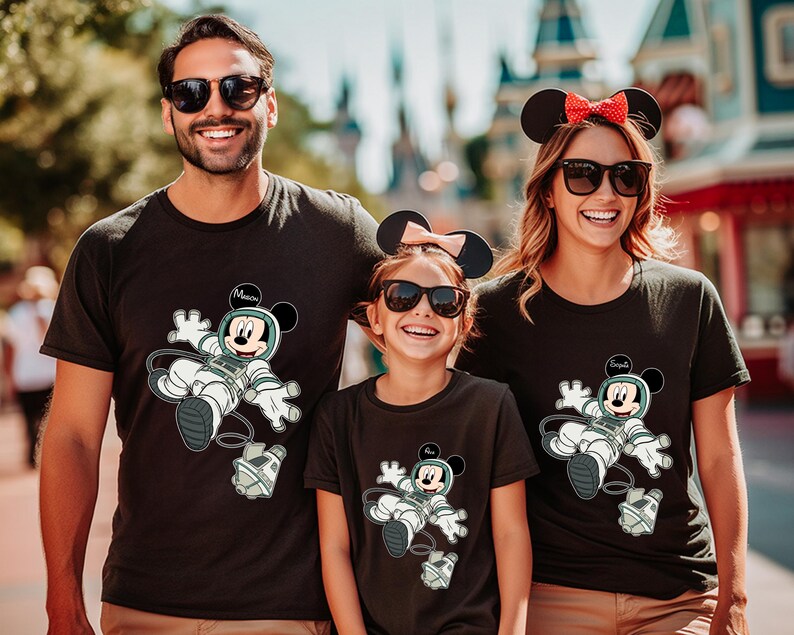 Peut inclure: Trois personnes portant des t-shirts noirs assortis avec un dessin anim&eacute; de Mickey Mouse en combinaison spatiale. Les chemises portent les noms "Mason" et "Emilia". La famille sourit et porte des lunettes de soleil.