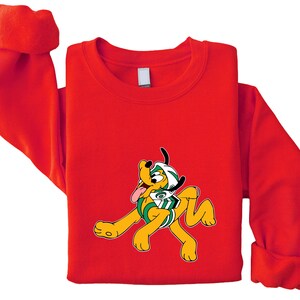 Peut inclure: Un sweat-shirt rouge avec un chien de dessin anim&eacute; portant un casque et un maillot de football. Le chien est jaune avec des oreilles noires et une langue rose. Le maillot est vert et blanc.