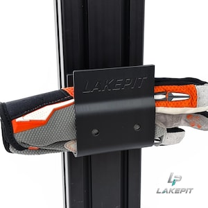 Könnte beinhalten: Eine schwarze Metallhalterung mit dem eingeprägten Wort LAKEPIT auf der Vorderseite, montiert an einer vertikalen schwarzen Aluminium-Profilschiene. Ein Paar graue, schwarze und orangefarbene Handschuhe steckt horizontal im gebogenen Rahmen.
