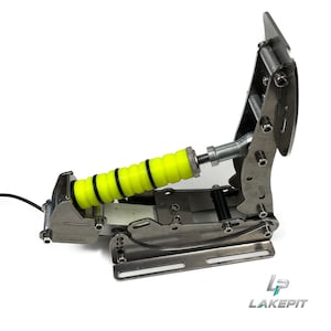 Puede incluir: Un pedal de simulador de carreras de metal con una placa vertical y un mecanismo de resorte horizontal con un parachoques acanalado de color amarillo neón brillante. El conjunto incluye componentes de acero plateado, juntas tóricas negras y un cable negro. El logotipo LAKEPI T es visible.