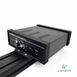 Puede incluir: Un amplificador de potencia negro ButtKicker BKA-130-CI con un panel de control frontal que incluye un botón de encendido, interruptor de filtro de corte bajo, perilla de frecuencia de corte alto, volumen y luces indicadoras de señal.