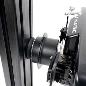 Può includere: Un adattatore per base del volante da corsa Fanatec nero montato su un profilo di estrusione in alluminio verticale. L'adattatore presenta un alloggiamento cilindrico con una flangia circolare e un logo con la scritta LAKEPIT in alto a destra.