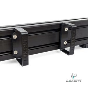 May include: A black aluminum extrusion rail featuring two attached black plastic brackets. Each bracket is secured with two silver metal screws and features the embossed text LAKEPIT on the side. The overall structure is matte black.