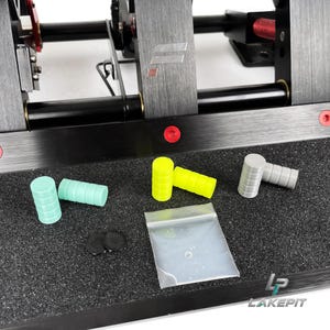 Könnte beinhalten: Ein Set zylindrischer Pedaleinsätze in Mintgrün, Neongelb und Grau, zusammen mit zwei kleinen schwarzen runden Scheiben und einem durchsichtigen Plastikbeutel, platziert auf einer schwarzen, texturierten Pedalbasis mit roten Schrauben.