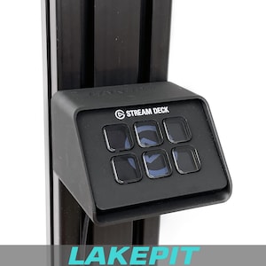 Könnte beinhalten: Ein schwarzes Stream Deck-Gerät mit sechs beleuchteten Tasten ist an einer schwarzen vertikalen Halterung befestigt. Das Stream Deck-Logo ist sichtbar. Das Wort "LAKEPIT" befindet sich am unteren Rand des Bildes.