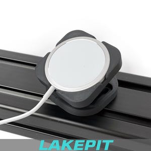 Puede incluir: Un soporte negro impreso en 3D sostiene un cargador inalámbrico blanco y plateado. El cargador está conectado a un cable blanco. El soporte está fijado a un riel metálico negro. La palabra "LAKEPIT" está en la parte inferior de la imagen.