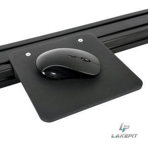 May include: A black computer mouse rests on a square black platform attached to a black aluminium extrusion rail. The platform is secured with two silver screws. The logo LAKEPIT is visible in the bottom right corner of the image.