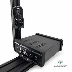以下が含まれることがあります： 黒いButtKickerパワーアンプBKA-130-C1。前面パネルには音量ノブ、信号インジケーター、リモートポートが備わっています。有線リモコンがユニット上部の垂直な黒いアルミニウム製レールに取り付けられています。