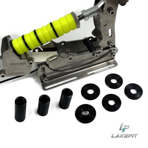 Könnte beinhalten: Eine Sim-Racing-Handbremse aus Metall mit einem leuchtend neongelben, gerippten Griff, einem silbernen Stahlrahmen sowie drei schwarzen zylindrischen Distanzstücken und vier schwarzen runden Unterlegscheiben, die unter dem Gerät liegen.