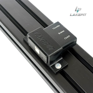 Könnte beinhalten: Eine schwarze Aluminium-Extrusionsschiene mit einem montierten schwarzen Steuermodul, auf dessen Oberseite die Wörter Throttle, Brakes und Clutch aufgedruckt sind. Das Modul zeigt den Markennamen LAKEPIT und einen silbernen USB-Anschluss.