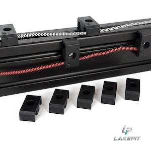 Puede incluir: Un riel de extrusión de aluminio negro con una correa dentada blanca y un cable trenzado rojo. Varios clips de montaje de plástico negro con las letras LP están unidos al riel, con cinco clips idénticos adicionales colocados debajo.