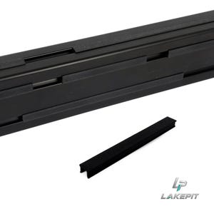 Puede incluir: Un riel metálico rectangular largo de color negro que presenta una serie de inserciones de goma negra texturizada espaciadas uniformemente a lo largo. Una pieza de inserción de goma negra a juego y separada se sitúa frente al riel.