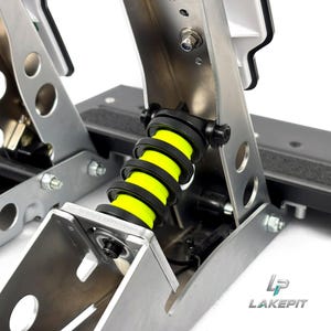 Könnte beinhalten: Ein Rennpedal-Set mit einem leuchtend neongelben Schraubenfeder-Mechanismus, der zwischen gebürsteten silbernen Metallstützen montiert ist. Die Baugruppe umfasst schwarze Beschläge, kreisförmige Ausschnitte und den Text LAKE PIT in der Ecke.