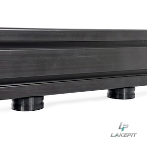 Könnte beinhalten: Ein schwarzes Aluminium-Extrusionsprofil mit linearem Kanaldesign, das auf zwei zylindrischen schwarzen Füßen steht. Das Bauteil hat eine glatte, matte Oberfläche und enthält den Logo-Schriftzug LAKEPIT in der unteren rechten Ecke.