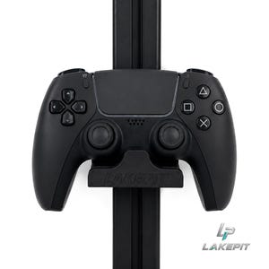 Könnte beinhalten: Ein mattschwarzer Videospiel-Controller, der auf einem vertikalen schwarzen Ständer montiert ist. Der Controller verfügt über ein zentrales Touchpad, zwei Analogsticks, ein Steuerkreuz und vier Aktionstasten mit Dreieck-, Quadrat-, Kreis- und Kreuzsymbolen.