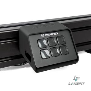 May include: A black matte plastic mount for a Stream Deck device, featuring a six-button layout with a glossy finish. The mount is attached to a black horizontal rail and has the word LAKEPIK embossed on the top edge and a logo in the corner.