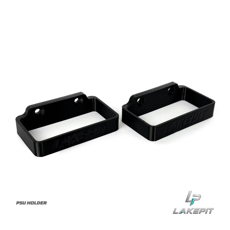 May include: Two black rectangular PSU holder brackets made of rigid material. Each bracket features two circular mounting holes along the top edge and the embossed text LAKEPIE on the front side. The design is open-ended for mounting purposes.