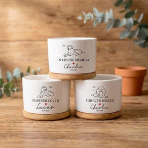 May include: Three white ceramic planters with bamboo saucers. Each planter features a different dog illustration and text: "In Loving Memory", "Forever Loved", and "Forever Missed". The planters are on a wooden surface.