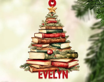 May include: A Christmas tree ornament shaped like a stack of books with a red star on top. The ornament is decorated with green leaves and red ornaments. The name "EVELYN" is printed on the bottom of the ornament.