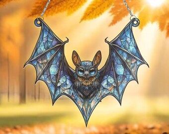 May include: A stained glass bat suncatcher with a blue and purple color scheme. The bat has a detailed design and is hanging from a silver chain.