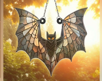 May include: A stained glass bat hanging in a window. The bat is black with yellow eyes and has a detailed, intricate design on its wings.