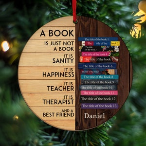 May include: A round wooden ornament with the text "A book is just not a book. It is sanity, happiness, teacher, therapist, and a best friend."  The ornament also features a stack of books with the text "The title of the book 1, The title of the book 2, The title of the book 3, The title of the book 4, The title of the book 5, The title of the book 6, The title of the book 7, The title of the book 8, The title of the book 9, The title of the book 10, The title of the book 11, The title of the book 12, The title of the book 13" and the name "Daniel".